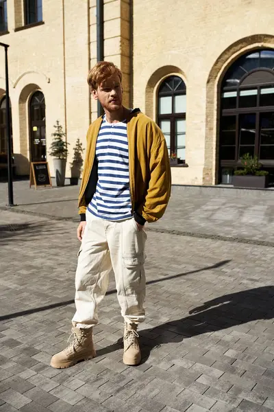 A debonair young man with red hair stands in front of an impressive building in the city. — Stock Photo