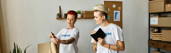 A young lesbian couple in volunteer t-shirts standing side by side, working together on a charity project. — Stock Photo