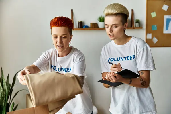 A young lesbian couple, wearing volunteer t-shirts, stands side by side, engaged in charity work together. — Stock Photo