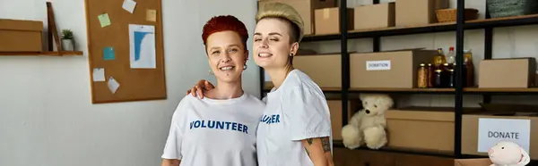 Zwei Frauen, ein junges lesbisches Paar in freiwilligen T-Shirts, stehen lächelnd zusammen und verkörpern Einheit und gemeinsamen Zweck. — Stockfoto