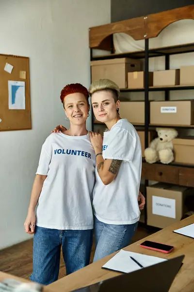 Дві молоді жінки у волонтерських футболках, що стоять поруч один з одним, працюють разом заради благодійності. — стокове фото