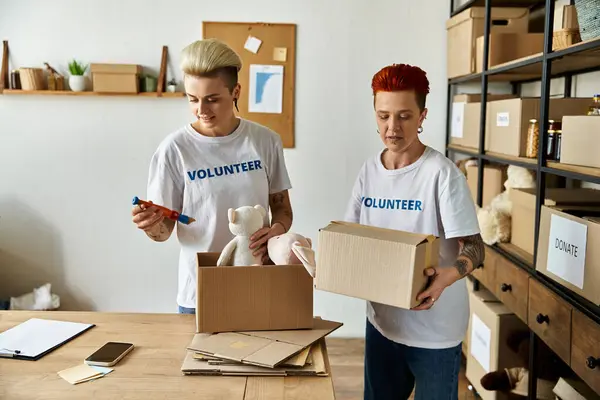 Ein junges lesbisches Paar in freiwilligen T-Shirts steht zusammen in einem Raum und arbeitet an karitativen Aufgaben. — Stockfoto