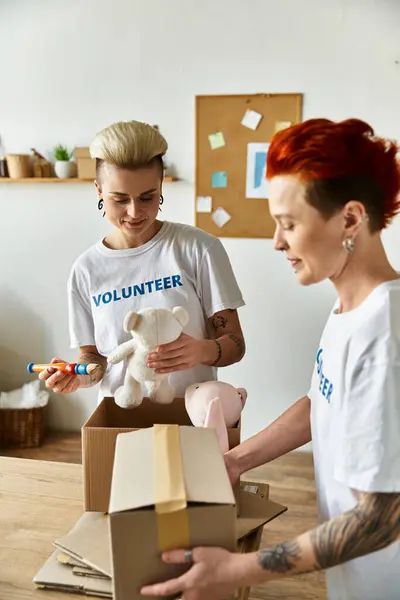 A woman in a volunteer t-shirt lovingly holds a teddy bear nestled in a cardboard box. — Stock Photo