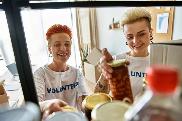 Ein lesbisches Paar in freiwilligen T-Shirts arbeitet leidenschaftlich zusammen, um durch Wohltätigkeit etwas zu bewirken. — Stockfoto