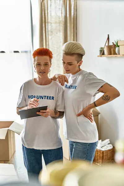 A young lesbian couple in volunteer t-shirts stand together, engaged in charity work, showing unity and empowerment. — Stock Photo