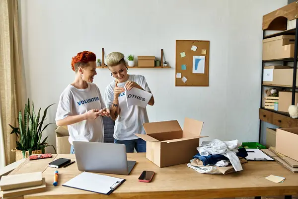 Una pareja, vistiendo camisetas voluntarias, colabora frente a una computadora portátil, comprometida y centrada en su trabajo caritativo. - foto de stock