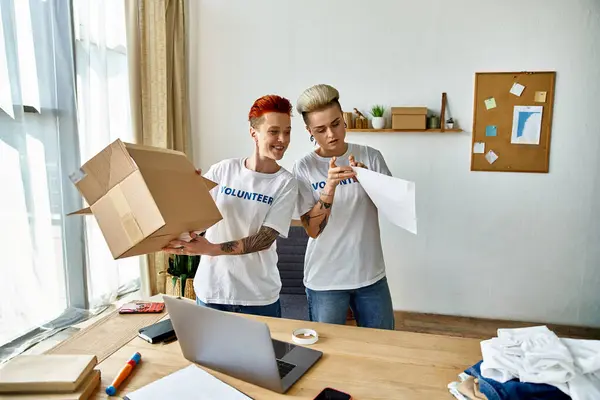 Una joven pareja lesbiana con camisetas voluntarias sosteniendo una caja de donaciones, trabajando juntos en caridad. - foto de stock