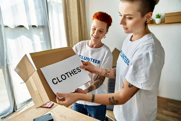 A young man and woman, a lesbian couple, in volunteer t-shirts hold a box of clothes for charity work together. — Stock Photo