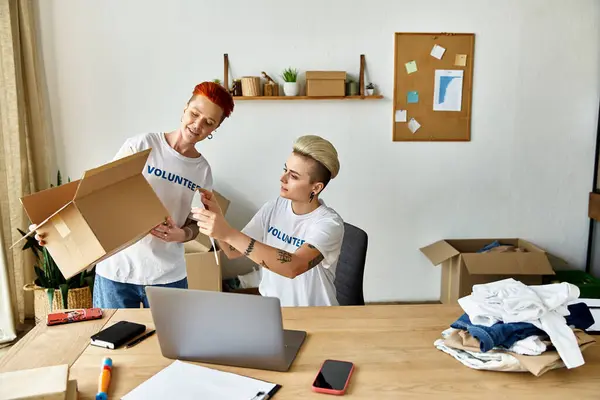 Women in volunteer t-shirts move boxes around a table with purpose and teamwork. — Stock Photo
