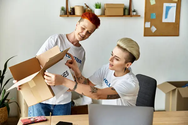 Two women in volunteer t-shirts stand at laptop, passionately working together. — Stock Photo