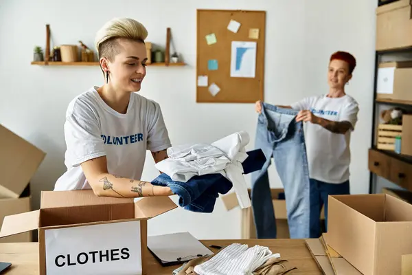 A young lesbian couple, wearing volunteer t-shirts, passionately unpack clothes together in a room. — Stock Photo