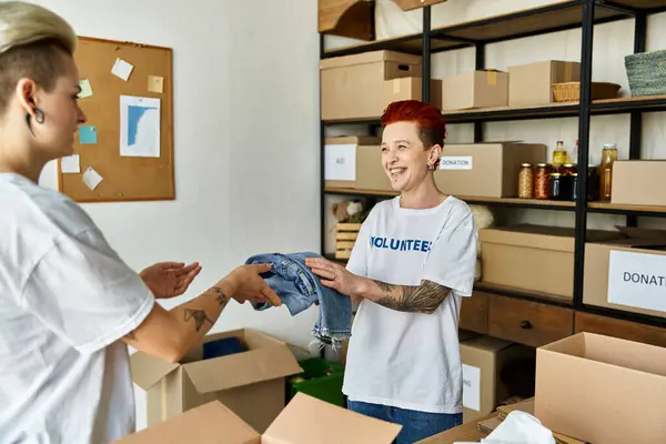 Lesbian woman hands shirt to her partner in volunteer scene. — Stock Photo