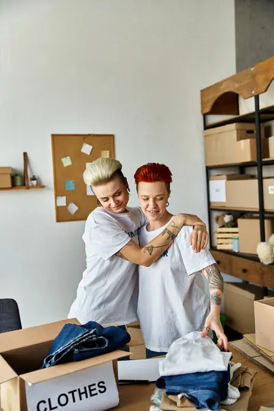 A young lesbian couple in volunteer t-shirts are standing together in a room, engaged in charity work. — Stock Photo