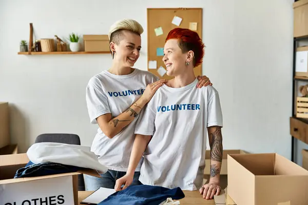 Young lesbian couple in volunteer t-shirts standing united in a room while doing charity work. — Stock Photo