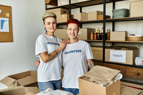 Junge lesbische Paare in freiwilligen T-Shirts stehen zusammen in einem Raum, vereint in wohltätiger Arbeit und Unterstützung. — Stockfoto