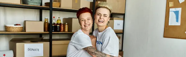Ein junges lesbisches Paar in freiwilligen T-Shirts steht zusammen in einem Raum und arbeitet an einem karitativen Projekt. — Stockfoto