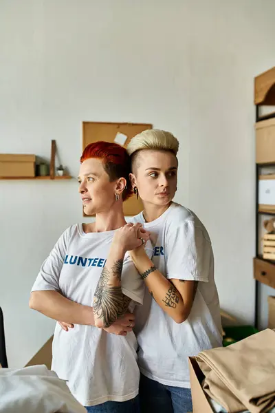 Молода пара лесбіянок у волонтерських футболках стоїть поруч у кімнаті, наповненій теплом і співчуттям. — стокове фото