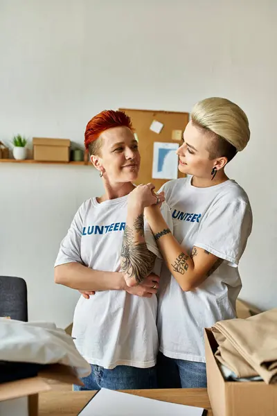A pair of women, part of the LGBTQ community, in volunteer t-shirts, standing next to each other, doing charity work. — Stock Photo
