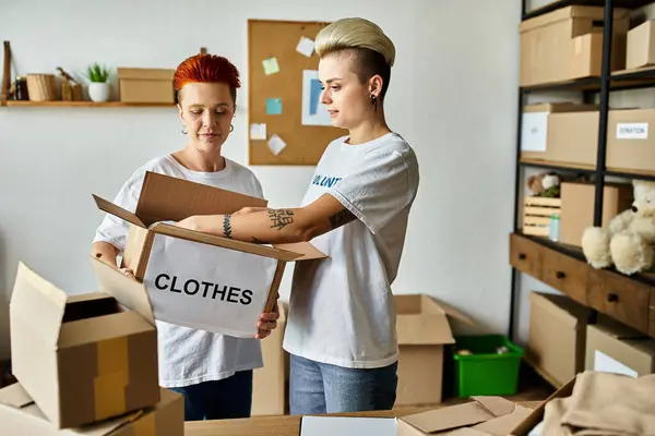 A young lesbian couple in volunteer t-shirts stand in a room with boxes, working together for charity. — Stock Photo