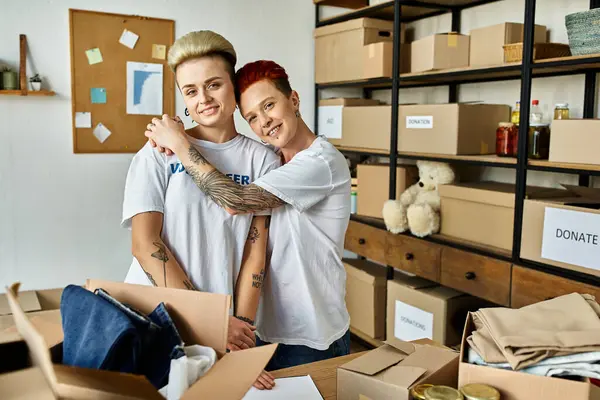 Молодая пара лесбиянок в волонтерских футболках, разделяющая теплые объятия во время совместной работы над благотворительным проектом. — стоковое фото