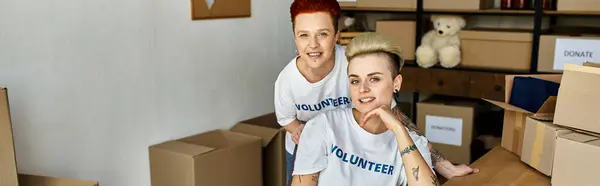 Young lesbian couple, donning volunteer t-shirts, passionately engaging in charity work together. — Stock Photo