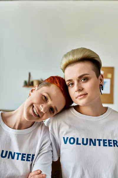Две молодые женщины, одна лесбийская пара, одетые в футболки добровольцев, стоят бок о бок, воплощая единство и служение. — Stock Photo