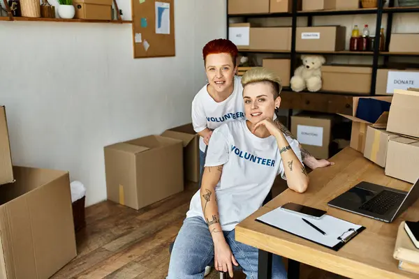 Two women in volunteer t-shirts stand in a room, passionately engaged in charity work together. — Stock Photo