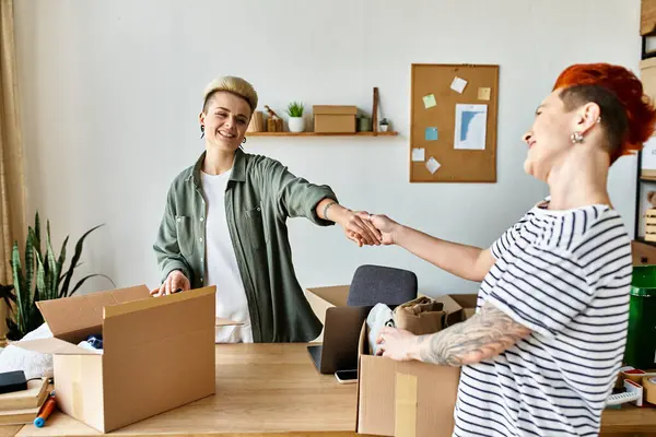 Two women shake hands in a room filled with donation boxes, united in their charitable efforts. — Stock Photo
