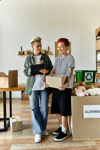 Young lesbian couple collaborating in a room filled with boxes for charity work. — Stock Photo