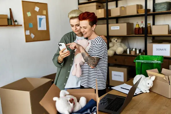 Young lesbian couple stand together in a room, working on a charity project with dedication. — Stock Photo