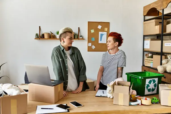 Молода лесбійська пара стоїть у кімнаті, наповненій коробками, об'єднаній у благодійну роботу. — стокове фото
