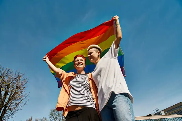 Una giovane coppia porta con orgoglio una bandiera arcobaleno, simbolo di amore e sostegno per la comunità LGBTQ. — Foto stock