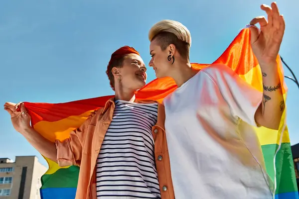 A young couple proudly stand together in front of a rainbow flag, celebrating love and unity in the LGBTQ community. — Stock Photo