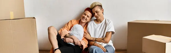 A young lesbian couple sitting closely together in a volunteer center surrounded by boxes, embodying unity and support. — Stock Photo
