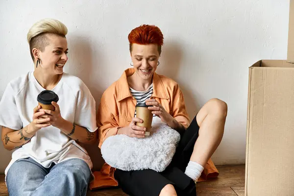 Two young women, a lesbian couple, sit on the ground in a volunteer center among boxes, engaged in charity work. — Stock Photo