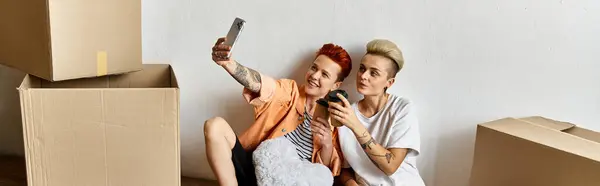 Young lesbian couple seated on a box, taking a break at a volunteer center surrounded by charity boxes. — Stock Photo