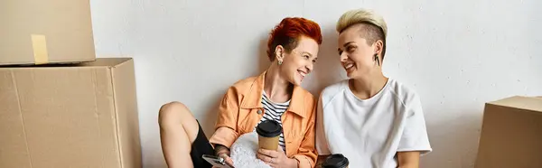 Giovane coppia lesbica sedersi fianco a fianco in un centro di volontariato, circondato da scatole di beneficenza. — Foto stock