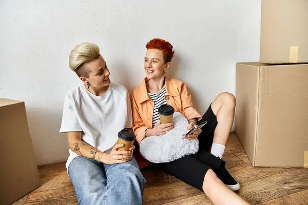A young lesbian couple sitting side by side in a volunteer center surrounded by boxes for charity work. — Stock Photo