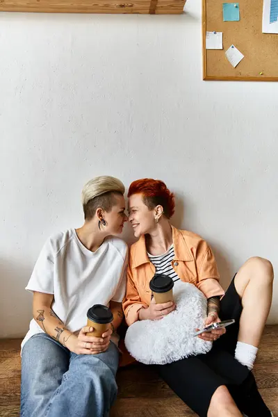 A young lesbian couple taking a break on top of a wooden bench in a volunteer center surrounded by boxes. — Stock Photo