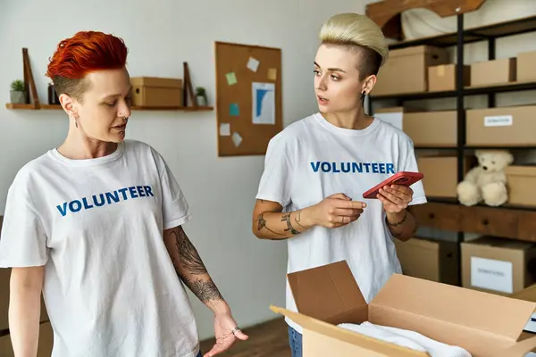 Ein junges lesbisches Paar, beide in freiwilligen T-Shirts, steht Seite an Seite, vereint in ihren Bemühungen für wohltätige Zwecke. — Stockfoto