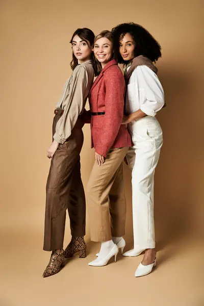 Multicultural women in stylish attire stand united, showcasing friendship and diversity against a beige backdrop. — Stock Photo