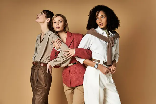 Tre belle donne multiculturali in elegante abbigliamento posare insieme su uno sfondo beige, in mostra la diversità e l'amicizia. — Foto stock