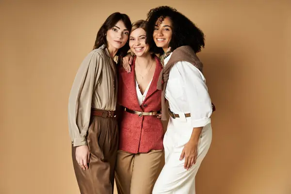Diverse young women in stylish attire stand united, showcasing friendship and cultural diversity on a beige background. — Stock Photo