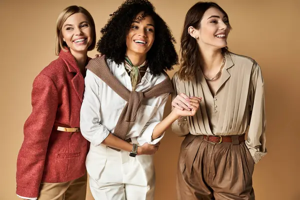 Three young, stylish, multicultural women stand together on a beige background. — Stock Photo
