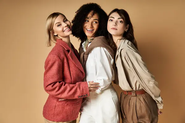 Tre giovani, belle donne di culture diverse posano insieme in abiti eleganti su uno sfondo beige. — Foto stock