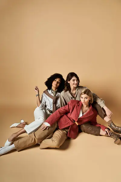 Multicultural women sit on ground, embracing unity and friendship in stylish attire. — Stock Photo