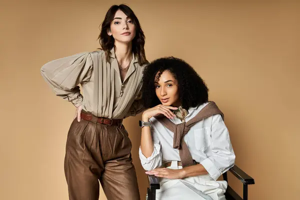 Two young, beautiful women in stylish attire pose gracefully together on a beige backdrop, symbolizing friendship and diversity. — Stock Photo