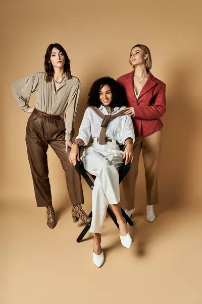 Three young, beautiful multicultural women in stylish attire standing next to each other on a beige background, embodying friendship and diversity in cultures. — Stock Photo