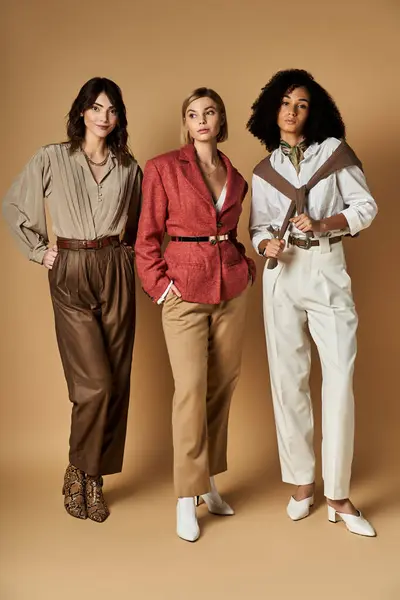 Three young, beautiful, multicultural women in stylish attire posing together on a beige background. — Stock Photo