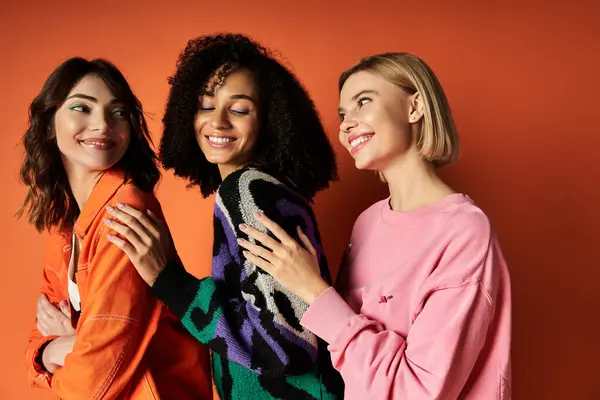 Young multicultural women in vibrant clothing stand together against an orange wall, exuding confidence and friendship. — Stock Photo